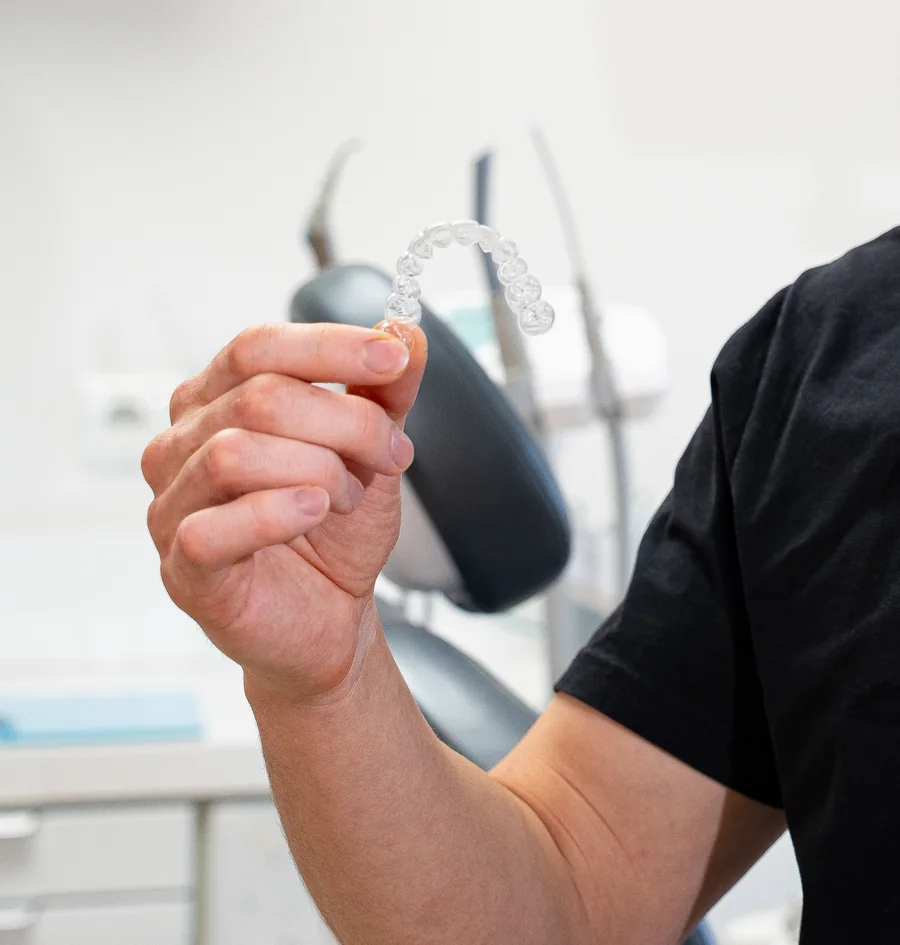 Eine transparente Aligner-Schiene in der Hand, im Behandlungszimmer