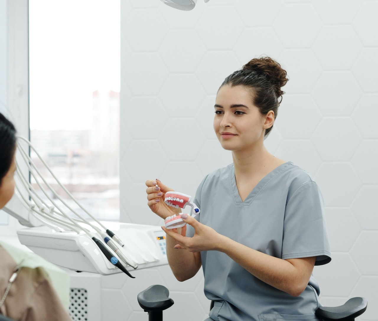 Zahnmedizinische Fachangestellte erklärt einer Patientin im Behandlungszimmer etwas am Kiefermodell